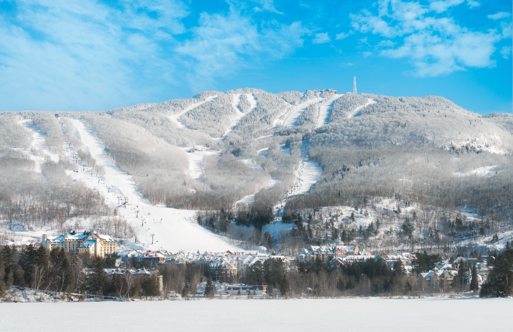 Cara nevada de Mont Tremblant con pistas, telesillas, pueblo peatonal y lago helado